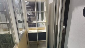 A small room with a blue floor, a trash bin with a green lid, and a white wall with a window.
