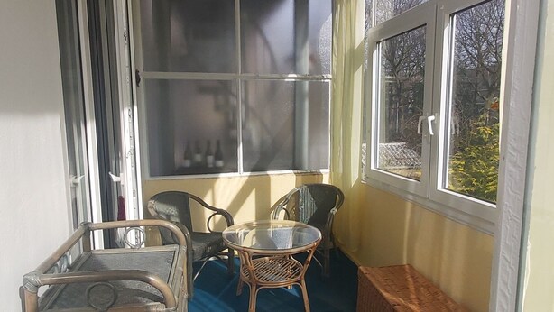 A sunlit room with a blue carpet, wicker furniture, and a large window.