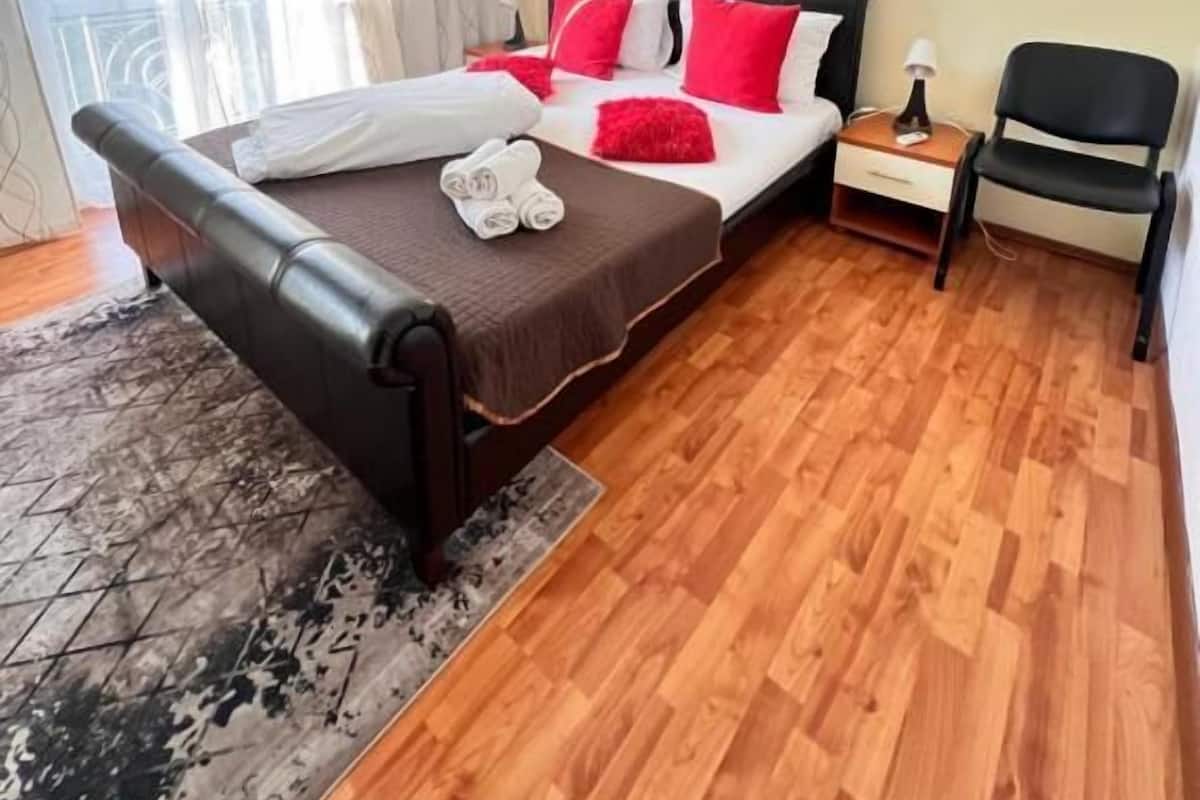 Un dormitorio con cama, mesitas de noche, una silla, alfombra y ventana con cortinas.