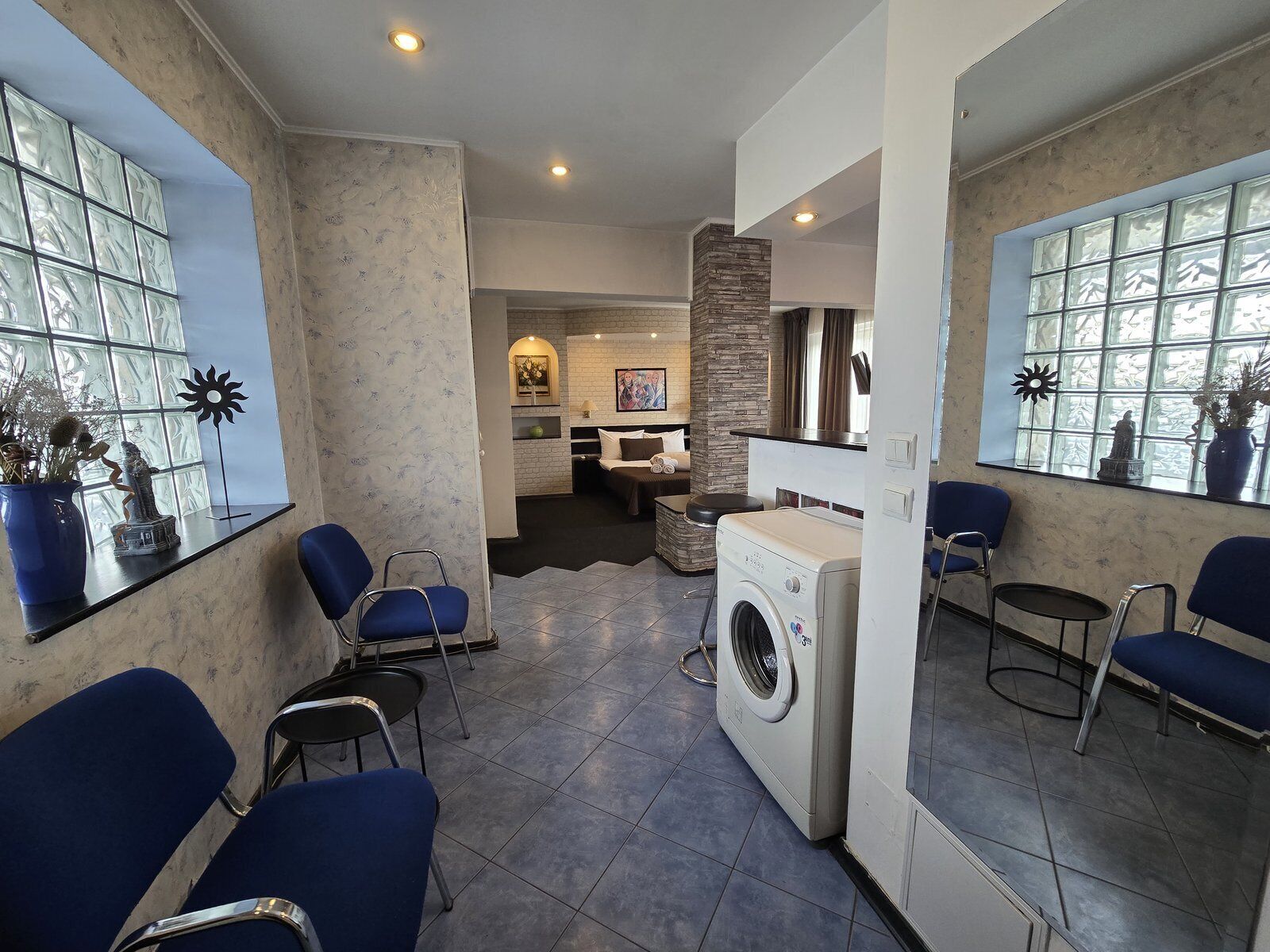A modern room with a washing machine, blue chairs, and a large window with decorative glass panels.