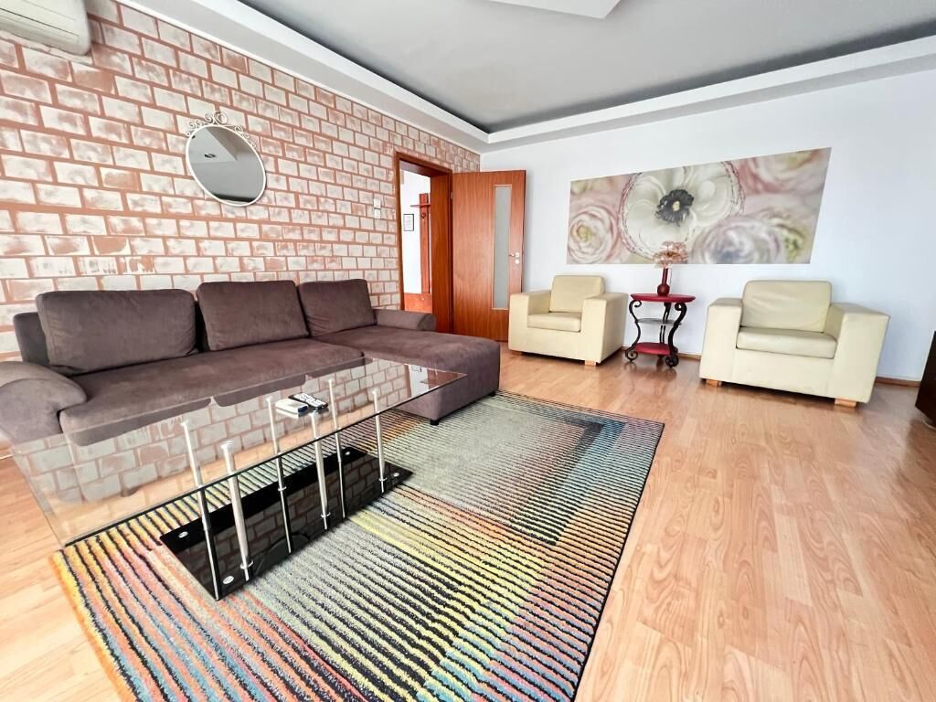 A living room with a brick wall, a sectional sofa, two armchairs, a coffee table, and a colorful rug.