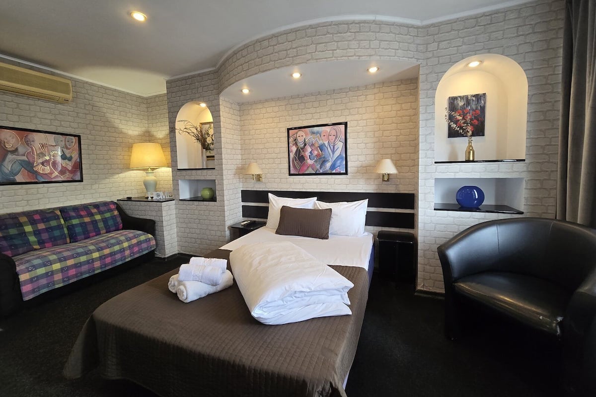 Una habitación de hotel con cama, sofá, sillón y escritorio con lámpara.
