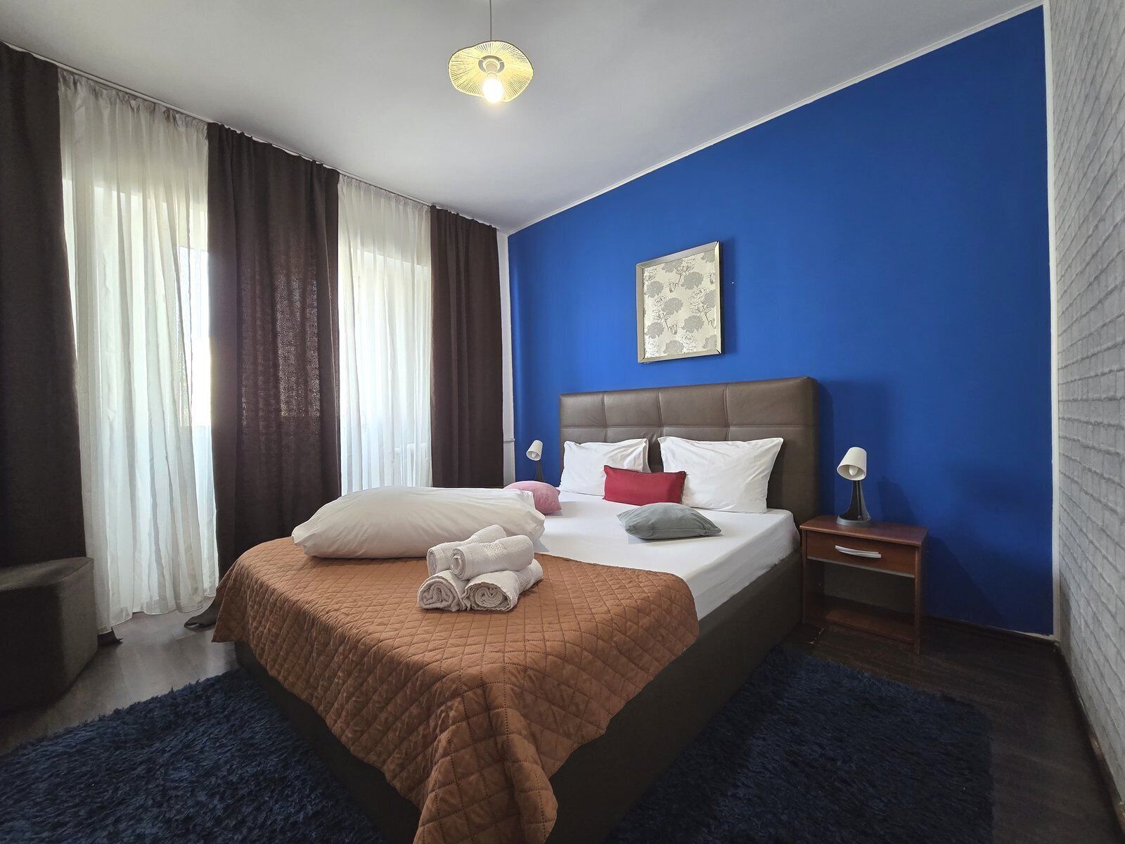 A hotel room with a large bed, a nightstand, a lamp, and a window with curtains.