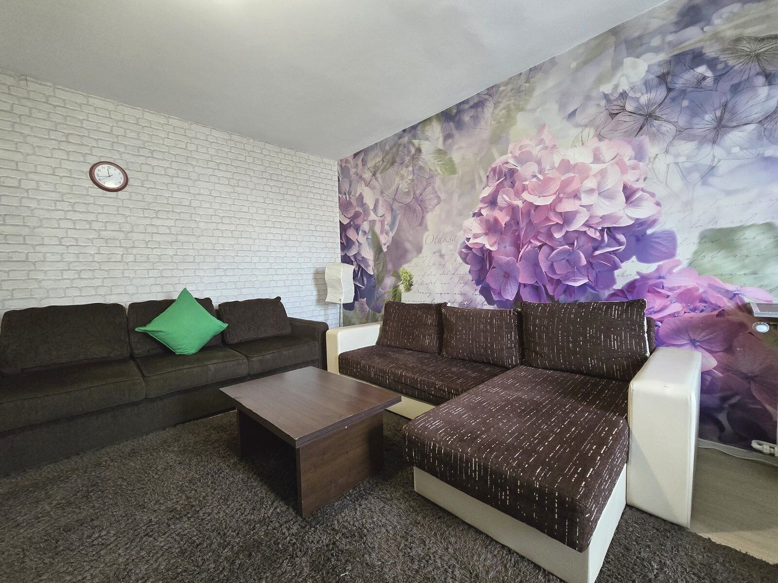 A living room with a white brick wall, two sofas, a coffee table, and a floral mural.