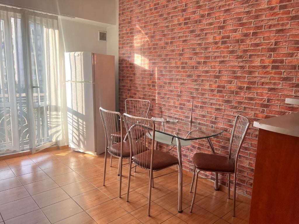 A dining area with a brick wall, a glass table, and metal chairs.