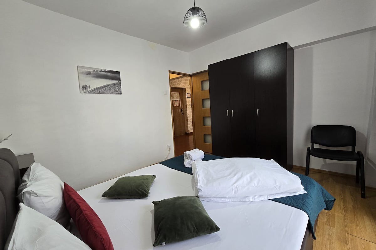 Un dormitorio con cama, almohadas, una silla, un armario y un cuadro en la pared.