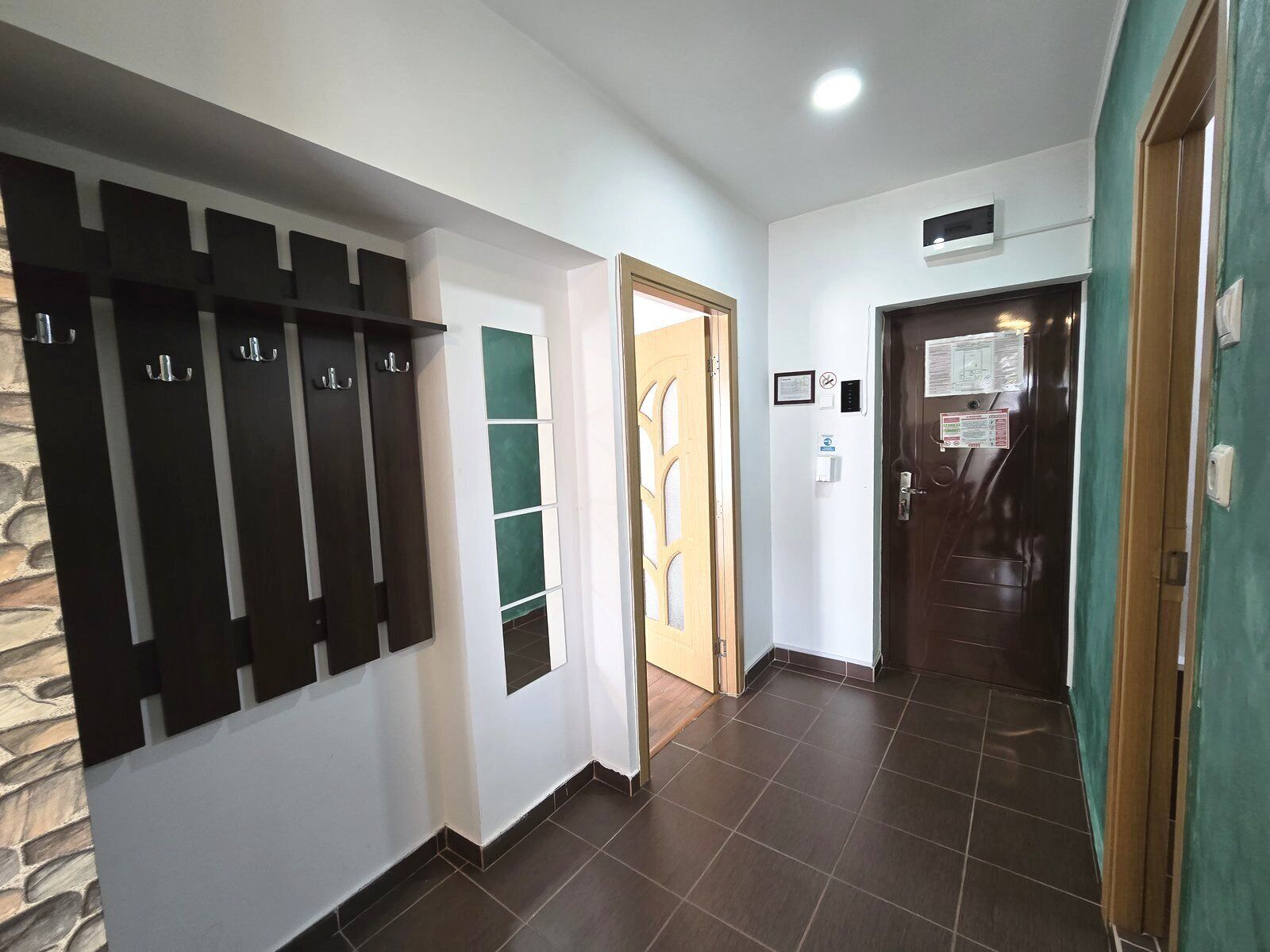 A hallway with a coat rack, a door with a sign, and a tiled floor.