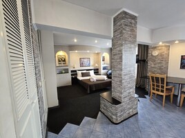 Una habitación de hotel moderna con una cama grande, una zona de estar con una mesa y sillas, y una pared decorativa de piedra.