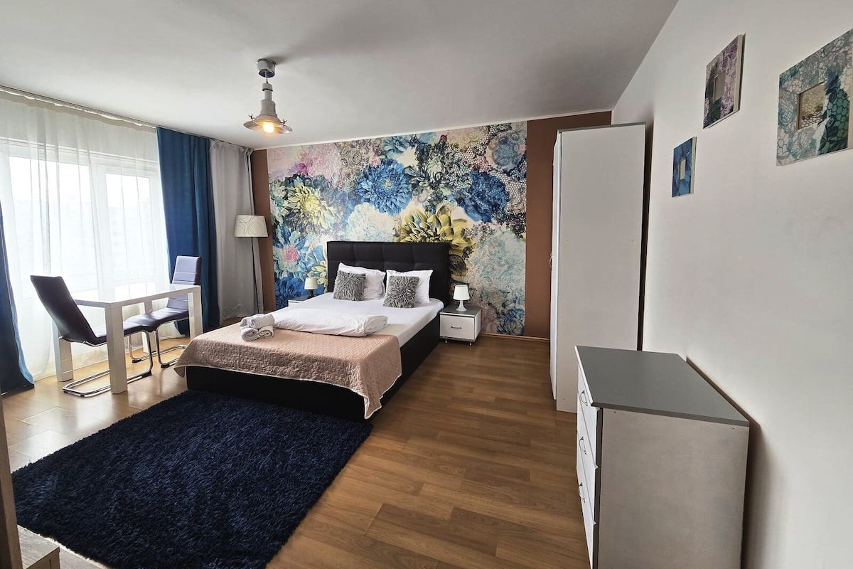 Una habitación de hotel con cama, escritorio, silla, mesita de noche y armario.