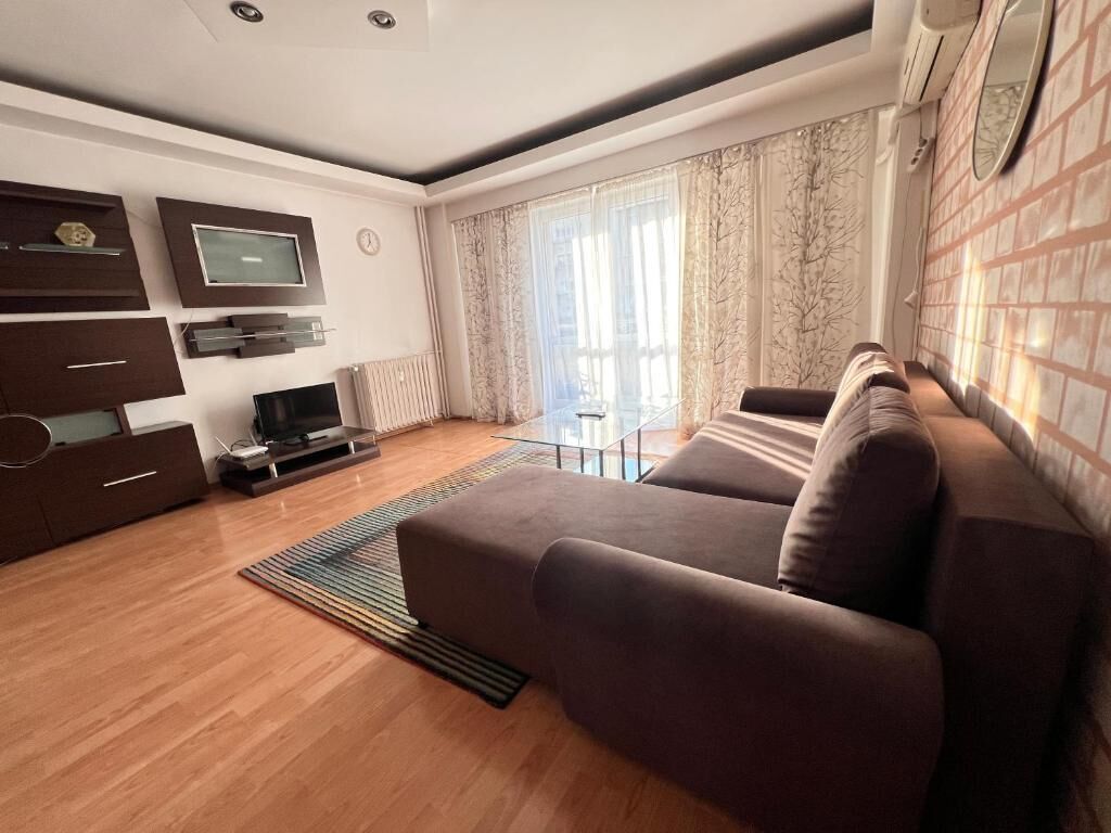 Una sala de estar moderna con un sofá marrón grande, un televisor de pantalla plana montado en la pared y una mesita con una lámpara.