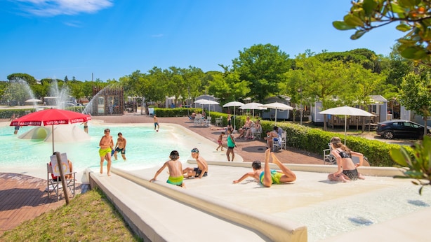 A swimming pool area with multiple water features, umbrellas, and lounge chairs. - Great Mobile Home in Cesenatico (Cesenatico)