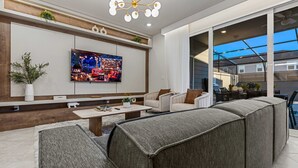 Een moderne woonkamer met een grote flatscreen televisie, comfortabele zitplaatsen en uitzicht op het buiten.