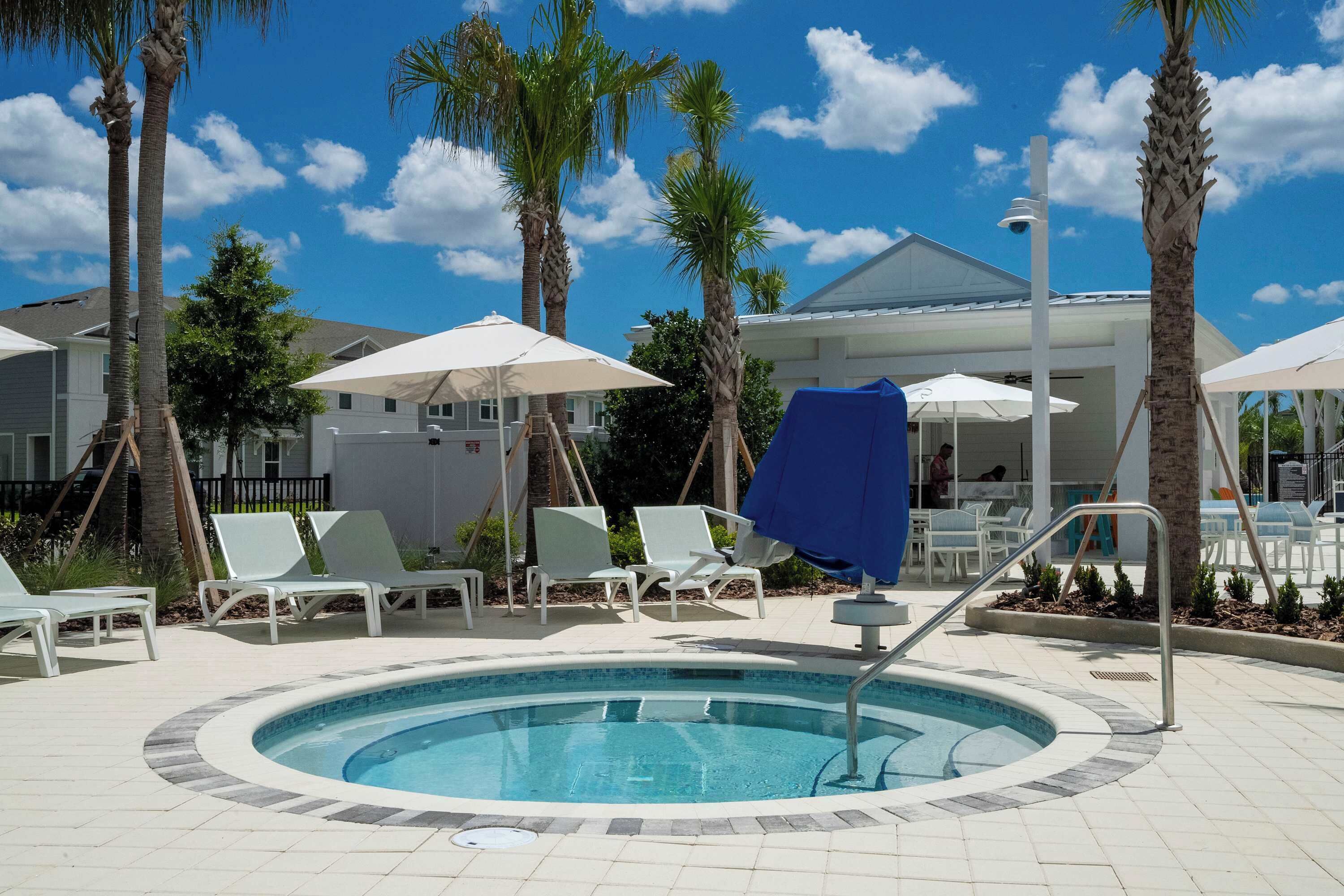 A pool area with lounge chairs and umbrellas, surrounded by palm trees and a building in the background.
