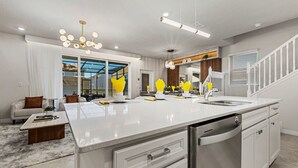 Een moderne keuken met een groot eiland, witte kasten en een roestvrijstalen vaatwasser.