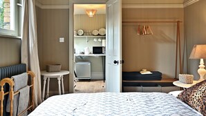 Un dormitorio con cama, mesita de noche, lámpara, armario y una pequeña mesa con una cesta.