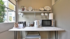 Una cocina con cubierta blanca, un microondas, una tetera y distintos utensilios y vajilla.