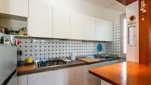 Uma cozinha com armários brancos, painel de azulejos, fogão a gás e bancada de madeira.
