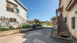 Rua residencial com pavimentação, escadaria que dá para um edifício e cerca com vegetação.