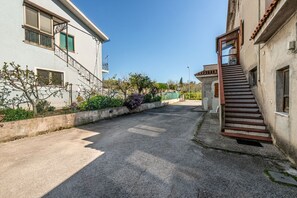 Eine Wohnstraße mit befestigter Straße, einer Treppe, die zu einem Gebäude führt, und einem Zaun mit Pflanzen.