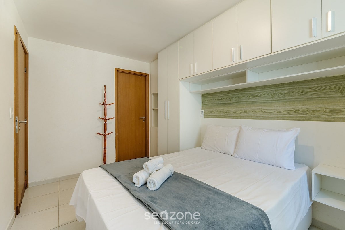 Quarto com uma cama, um cabideiro de madeira e armários brancos.