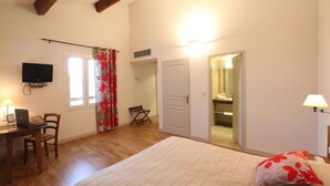A bedroom with a bed, a desk with a laptop, a television, and a door leading to a bathroom. - Domaine les Mejeonnes (Valaurie)