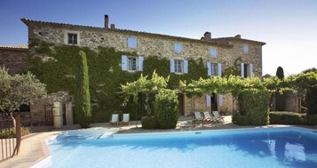 Un edificio de piedra con piscina, dos sillones de descanso y una pérgola.