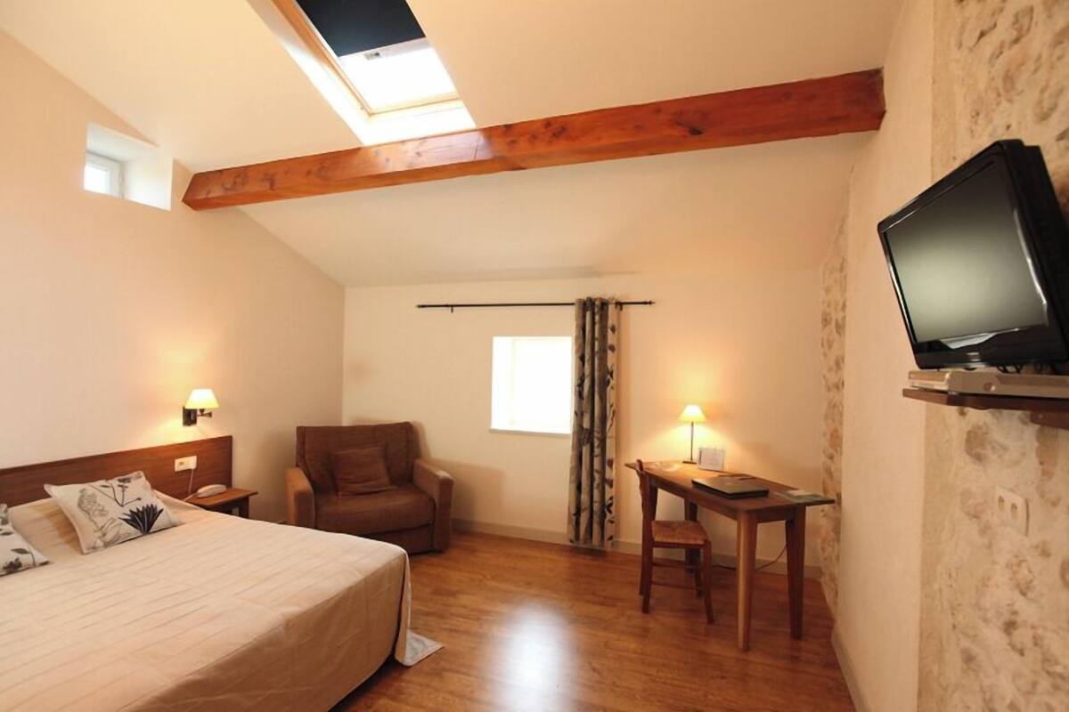 Una habitación de hotel con cama, escritorio, silla, televisor y tragaluz.
