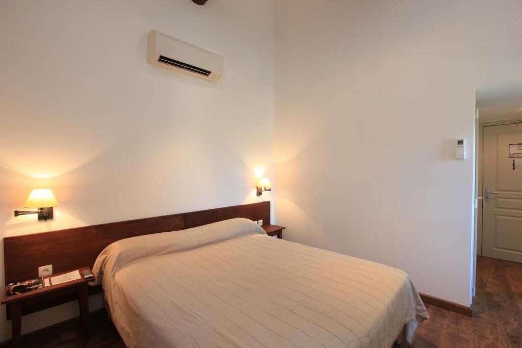 Habitación de hotel con cama, mesitas de noche, lámparas de pared y unidad de aire acondicionado.