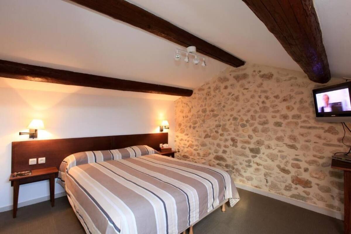 Habitación de hotel con pared de piedra, una cama con ropa de cama a rayas, dos lámparas de noche y un televisor en la pared.
