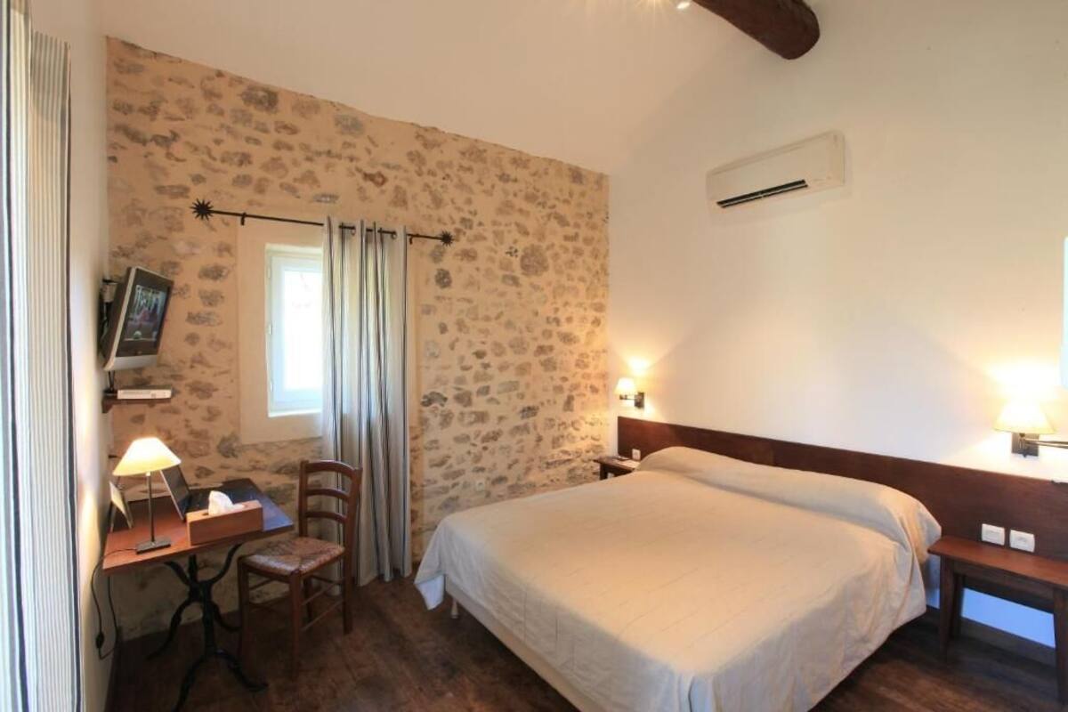 Un dormitorio con pared de piedra, una cama, un escritorio con lámpara y una silla.