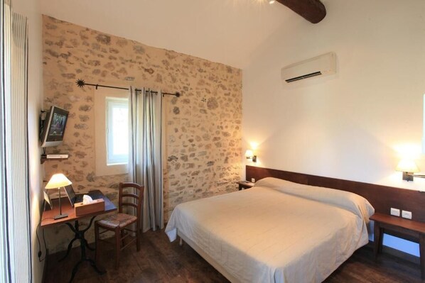 Un dormitorio con pared de piedra, una cama, un escritorio con lámpara y una silla.