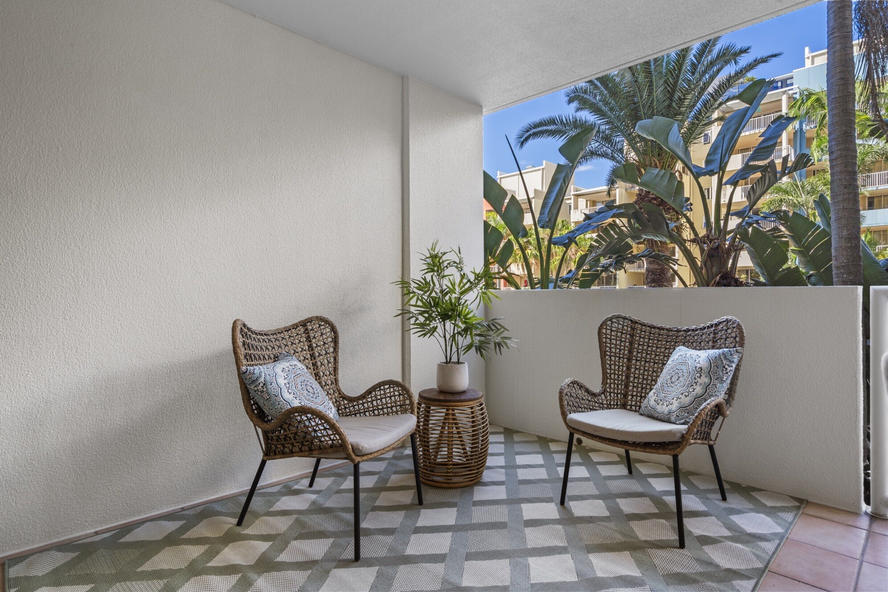A balcony with two wicker chairs, a small round table with a potted plant, and a patterned floor.