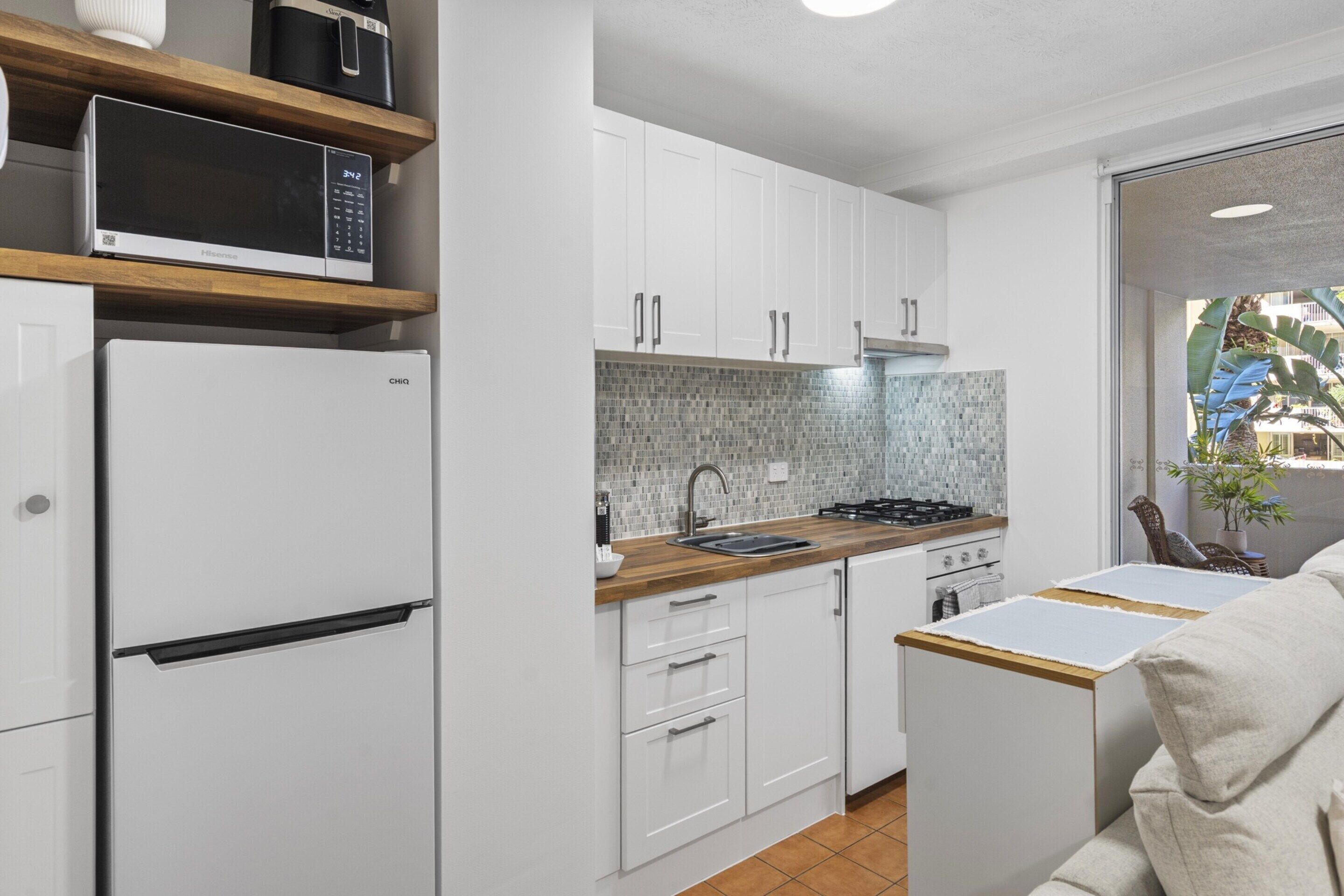 A compact kitchen with white cabinets, a microwave, a stove, and a sink.