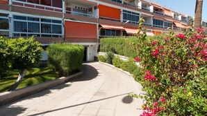 A multi-story building with balconies, a paved walkway, and lush greenery. - Cozy Maspalomas Bungalow With Pool (San Bartolomé de Tirajana)