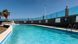 A swimming pool with clear blue water, surrounded by a stone wall and a blue fence. - Cozy Maspalomas Bungalow With Pool (San Bartolomé de Tirajana)
