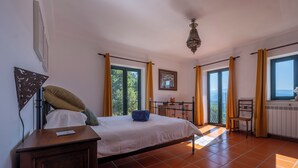 Une chambre à coucher comprenant un lit, une table de chevet, une commode, une fenêtre avec des rideaux, un lustre et une vue sur l’extérieur.
