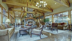 A spacious living room with a fireplace, wooden beams, and large windows.