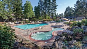 A pool area with two hot tubs, lounge chairs, and a large swimming pool surrounded by trees and rocks.