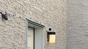 Pared exterior con textura, una puerta y una lámpara fijada a la pared.
