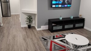 Una sala de estar moderna con un televisor de pantalla plana montado en la pared, un mueble de entretenimiento negro, una mesa de centro redonda blanca y una alfombra estampada.