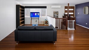Een moderne woonkamer met een zwarte bank, een televisie op een dressoir, houten vloeren en een trap met een leuning.