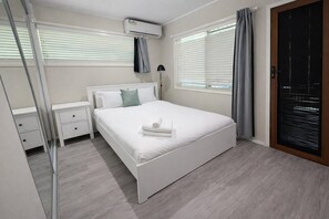Een moderne slaapkamer met een bed, nachtkastjes, een spiegel en een raam met zonwering.