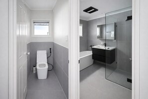 Een moderne badkamer met toilet, bidet en een douchecabine met glazen wanden.
