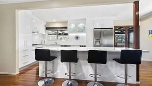 Een moderne keuken met witte kasten, een centraal eiland met barkrukken, roestvrijstalen apparatuur en uitzicht op de omgeving.