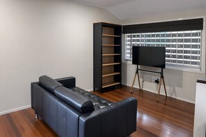 Een moderne woonkamer met een zwarte leren bank, een zwarte entertainementunit en een groot raam met jaloezieën.