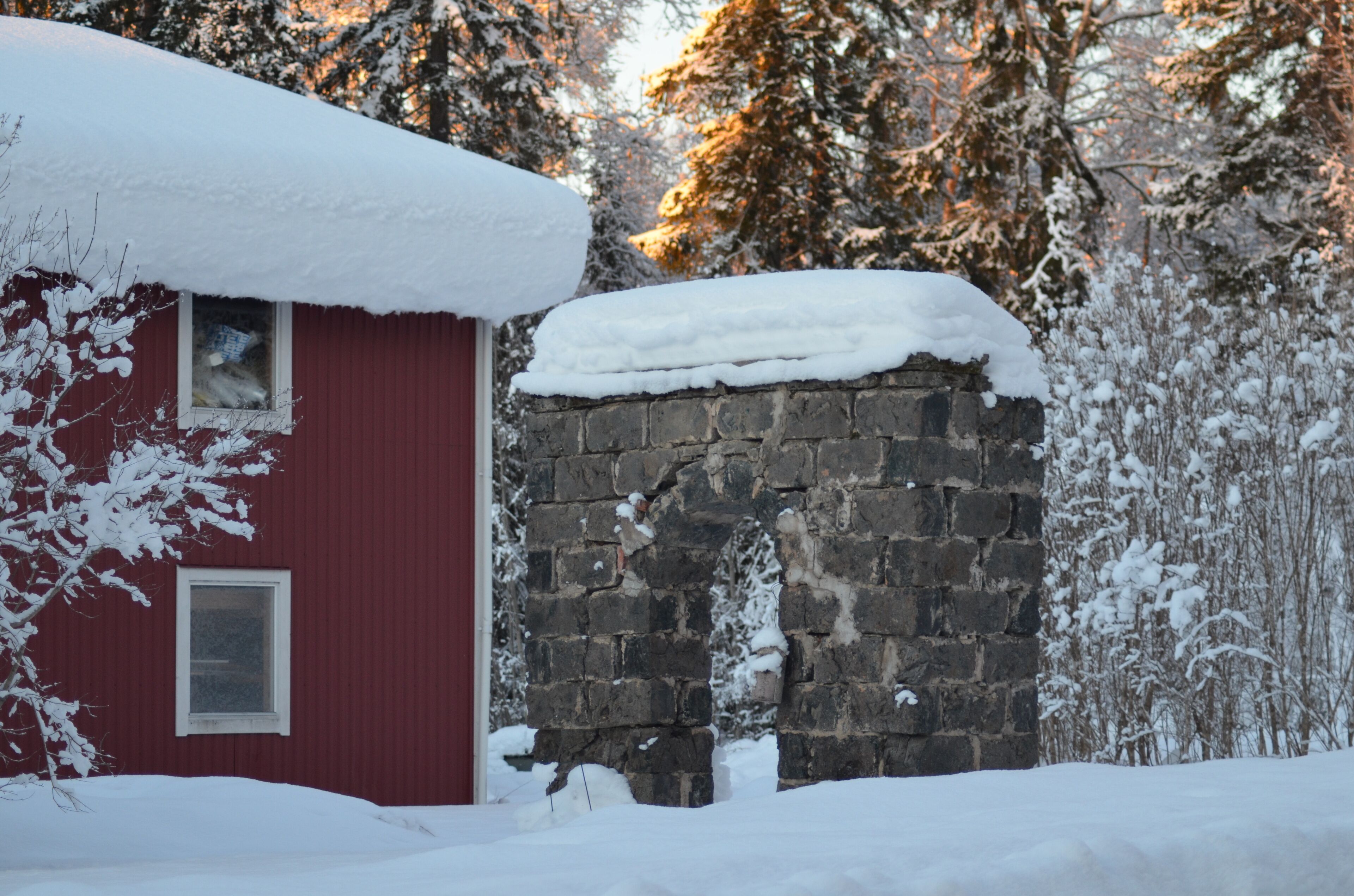 A red building with a stone archway, surrounded by snow-covered trees.