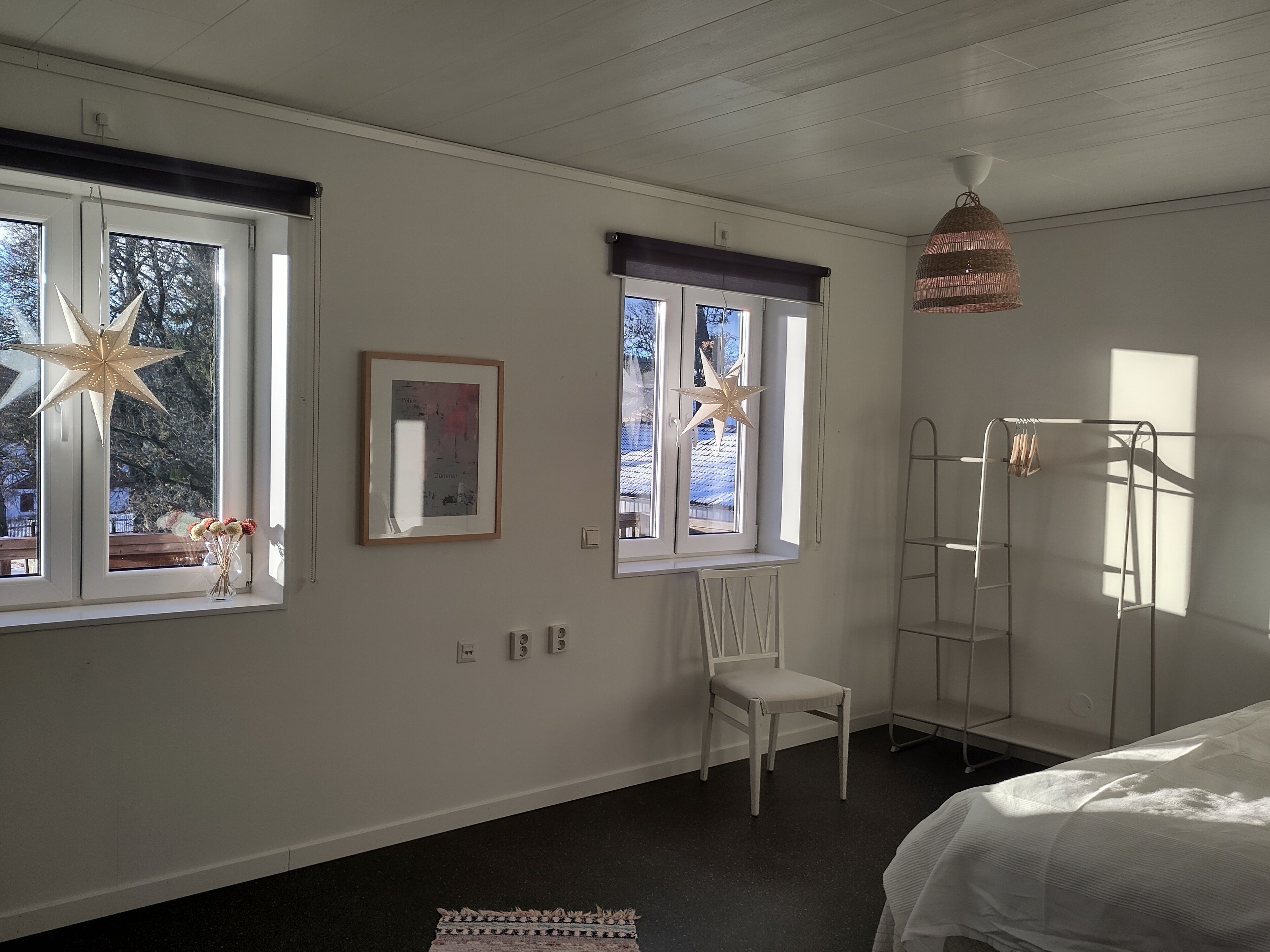 A bedroom with two windows, a bed, a chair, a ladder, and a hanging light fixture.