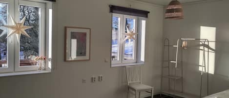 A bedroom with two windows, a bed, a chair, a ladder, and a hanging light fixture.