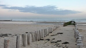 Ein Strand mit einer Holzpromenade, die zum Wasser führt, einem Pier im Hintergrund und einem bewölkten Himmel.
