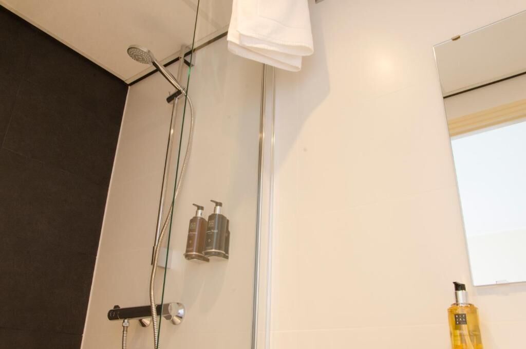 A modern bathroom with a glass shower enclosure, a towel hanging on the wall, and two bottles of toiletries.